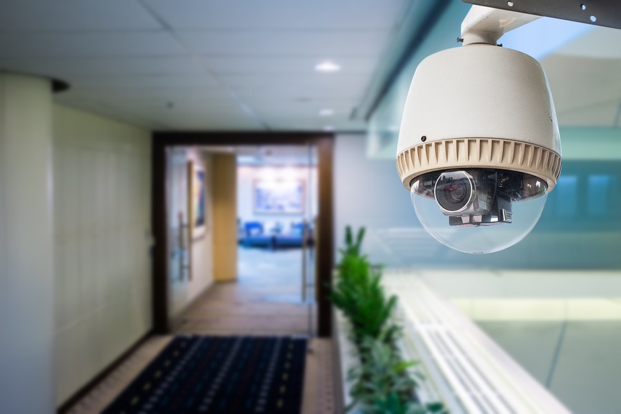 closeup shot of a commercial security camera with a hallway in the background behind it